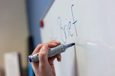 Abstrakte Illustration in den Farben Blau und Rot von zwei Personen auf einer Leiter an einer großen Glühbirne